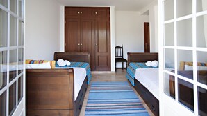 A hotel room with two wooden beds, a large wooden wardrobe, and a striped rug.
