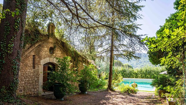 Ein rustikales Steinhaus mit Bogenportal, umgeben von üppiger Vegetation und einem klaren, blauen Pool.