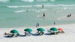 Uma praia com vários guarda-sóis verdes e cadeãs de praia, indicando um ambiente à beira-mar.