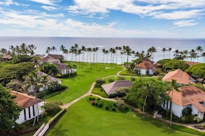An aerial view of a coastal resort with multiple houses, a well-maintained lawn, and a view of the ocean.