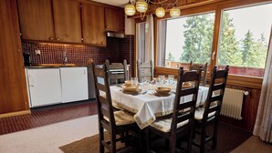 A dining area with a table set for four, wooden chairs, a white tablecloth, and a view of trees through large windows. - Located in Les Collons 1850, only 50 meters from the ski-lifts "La Joc" and "Petit Vallon" (crossbow (Thyon-Les Collons)
