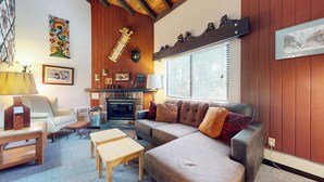 Een gezellige woonkamer met een open haard, houten wanden, een bank, een salontafel en een lamp.