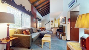 Een gezellige woonkamer met een bank, een houten salontafel en een televisie. Er is een eethoek met een tafel en stoelen, en een keuken met een koelkast en een fornuis.