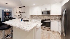 A modern kitchen with white cabinets, a granite countertop, stainless steel appliances, and a bar area with stools.