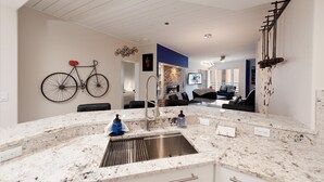 A modern kitchen with a marble countertop, stainless steel sink, and a bicycle mounted on the wall.