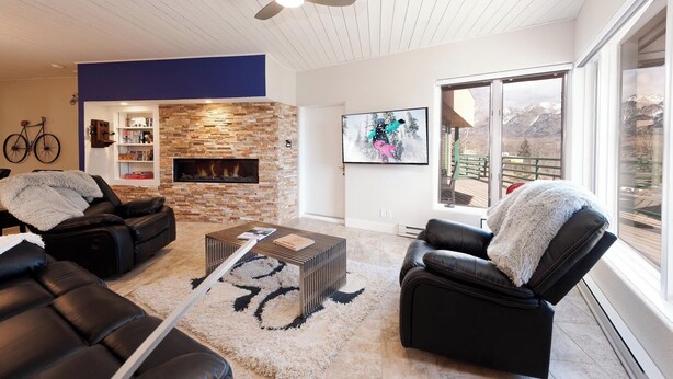A modern living room with a stone fireplace, leather sofas, a coffee table, and a large window offering a mountain view.