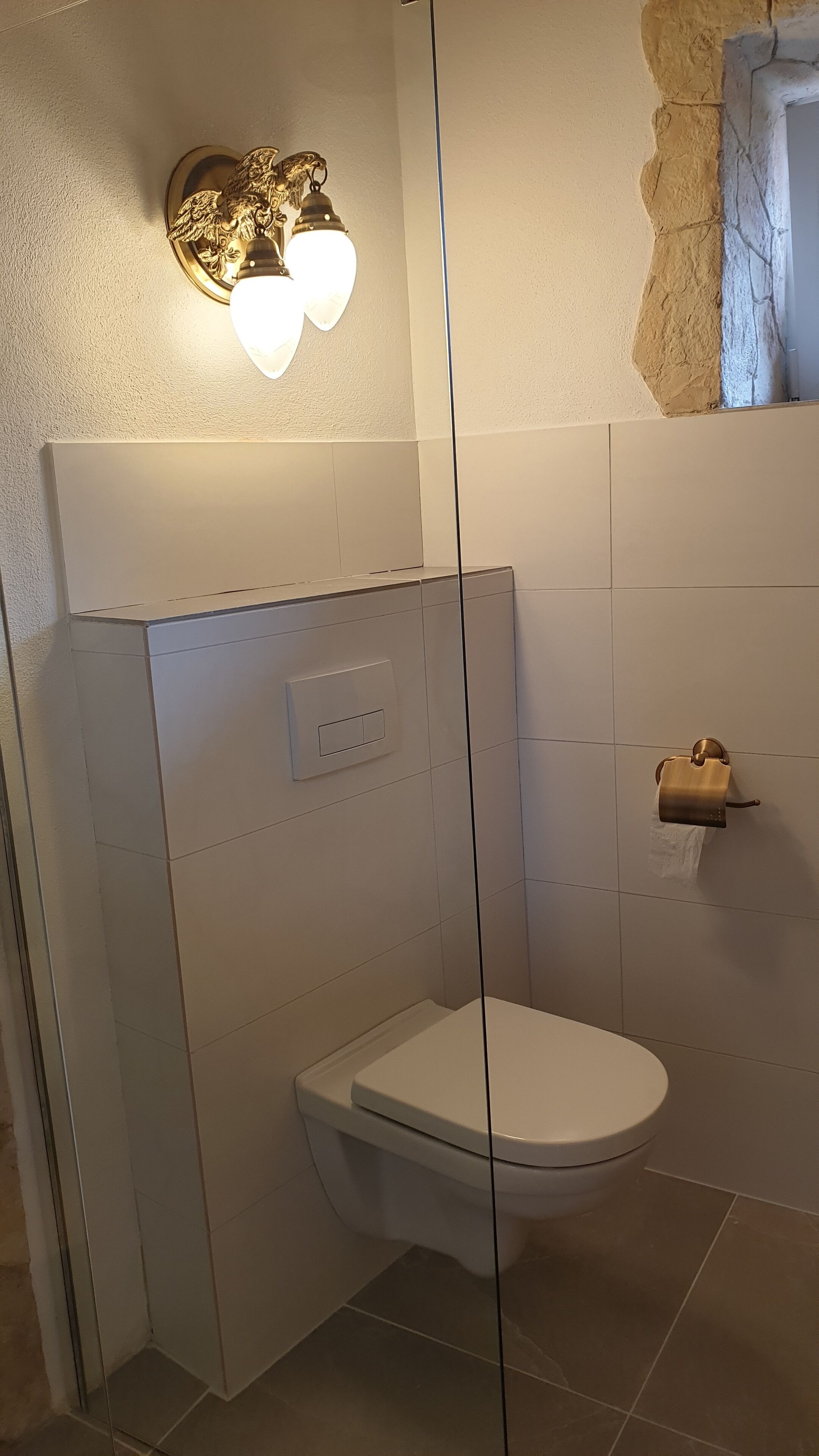 Ein kleines, separates Badezimmer mit Toilette, Wandleuchte und Handtuchspender.