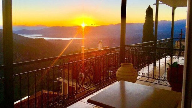 A balcony with a view of a sunset over mountains and a lake.