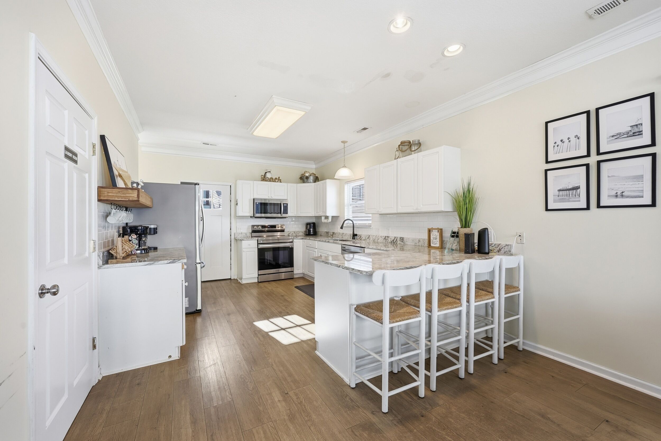A modern kitchen with white cabinetry, a central island with bar stools, a microwave, oven, and a sink.