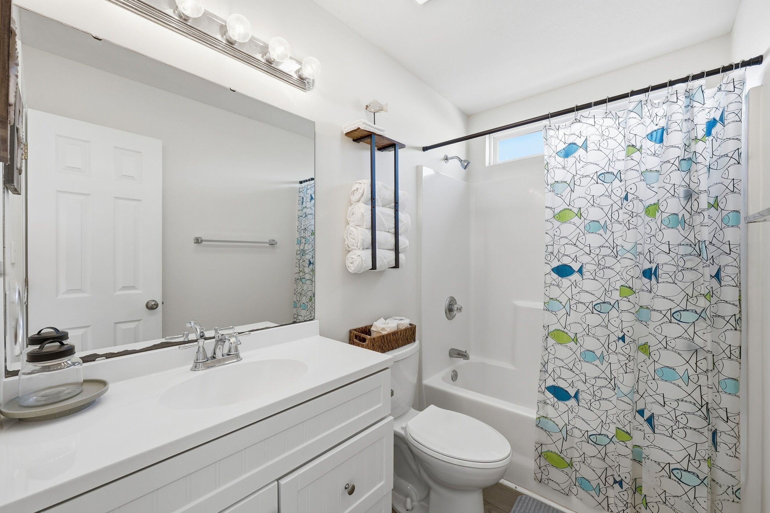 A modern bathroom with a white sink, mirror, and toilet. There is a shower curtain with a fish pattern.