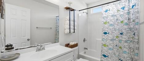 A modern bathroom with a white sink, mirror, and toilet. There is a shower curtain with a fish pattern.