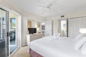 A hotel room with a large bed, a ceiling fan, a television, a dresser, and a sliding glass door leading to an outdoor area.