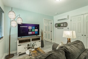 Una sala de estar con un televisor de pantalla plana, una mesa de centro de madera, un sofá gris y una lámpara.