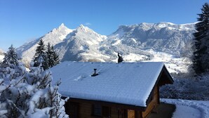 Une cabane en bois, dont le toit est recouvert de neige, entourée d’arbres et de montagnes enneigées.