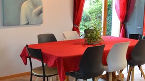 Un coin repas avec une nappe rouge, des chaises noires et blanches, une plante en pot et un tableau accroché au mur.