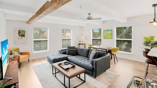 Un salon moderne avec un canapé d’angle, une table basse et un coin repas agrémenté d’une chaise jaune.