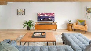Un salon moderne avec un meuble TV en bois, une grande peinture représentant un coucher de soleil, un canapé et une table basse.