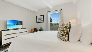 Une chambre à coucher avec un lit, un téléviseur posé sur une commode, une fenêtre avec des rideaux et un tableau encadré accroché au mur.