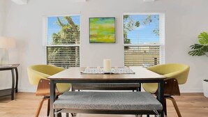 Un coin repas avec une table, deux chaises jaunes, un banc et un tableau accroché au mur.