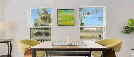 A dining area with a table, two yellow chairs, a bench, and a painting on the wall.