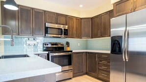 A modern kitchen with dark wooden cabinets, stainless steel appliances, and a light blue tiled backsplash. - The Grey Beach House!! In the heart of Grand Bend (Grand Bend)