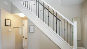 A staircase with a white handrail and black balusters, leading to a door with a light switch and a framed sign on the wall. - Easy Walk to Clifton Hill Falls & Attractions! (Niagara Falls)