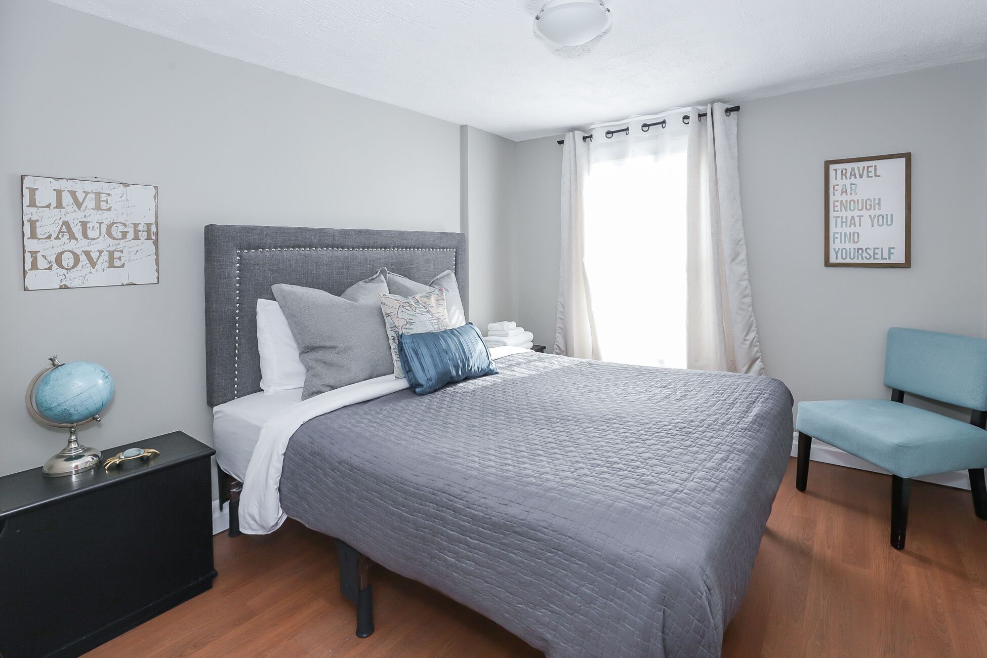 A bedroom with a grey bed, a nightstand, a globe, and a chair.