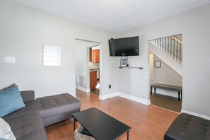 Un salon avec un canapé gris, une table basse noire et un téléviseur fixé au mur.