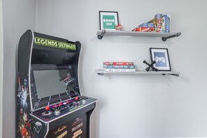 Une borne d’arcade sur le thème de Star Wars, un panneau encadré avec l’inscription « GAME ON », et des étagères remplies de jeux de société, ainsi qu’une manette de jeu encadrée.