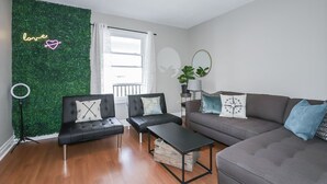 A modern living room with a green wall, two black sofas, a grey sofa, a small table, and a window with curtains. - Easy Walk to Clifton Hill Falls & Attractions! (Niagara Falls)