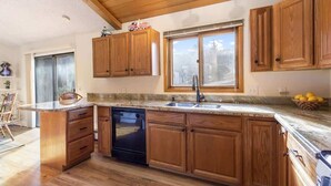 A kitchen with wooden cabinets, a granite countertop, a dishwasher, and a window with a view of trees.