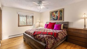 A bedroom with a wooden bed, a ceiling fan, a window, and a painting on the wall.