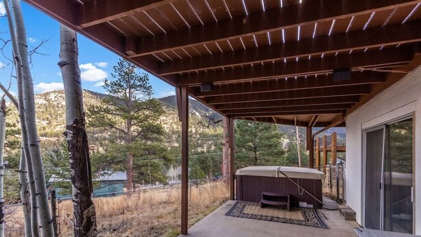 A covered patio with a hot tub, a table, and a view of a mountainous landscape.