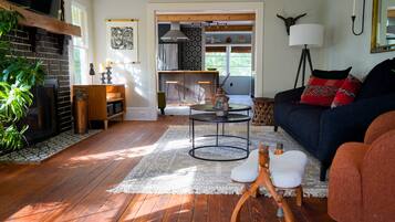 A cozy living room with a fireplace, a dining area, and a kitchen visible through an open doorway.