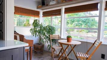 A sunroom with a wooden table and chairs, a potted plant, and large windows with blinds.