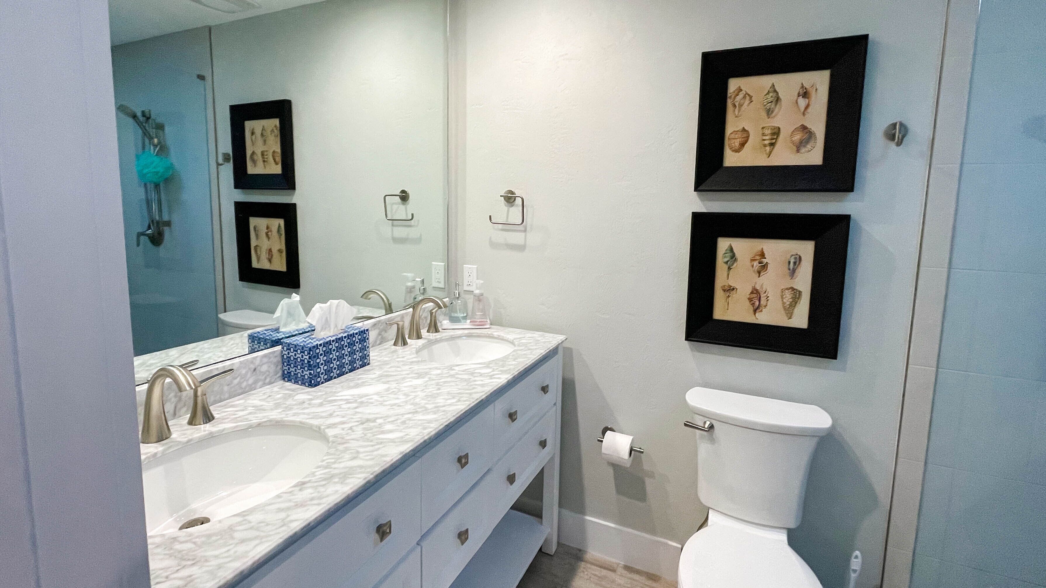 Une salle de bain avec deux lavabos, des toilettes et des tableaux encadrés au mur.
