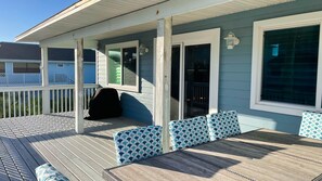 A covered deck with a table and chairs, a covered patio area, and a sliding glass door leading to a covered outdoor space. - Ultra Luxury beachside Beach House. Steps from the Ocean and Intercoastal. (New Smyrna Beach)