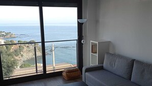 En moderne stue med en stor skydedør, der fører ud til en balkon med udsigt over havet.