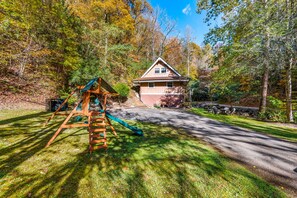 Surrounded by a lush lawn and trees, this two-story house offers a family-friendly atmosphere with a swing set and driveway leading to the front entrance.