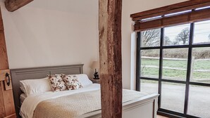 Ein Schlafzimmer mit einem großen Bett, Holzbalken, Blick ins Freie und einer rustikalen Holzsäule.