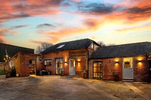 Ein Gebäude aus Backsteinen mit mehreren Fenstern und Türen, eine Schotterauffahrt und ein Sonnenuntergangshimmel.