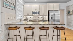 A modern kitchen with white cabinets, a granite countertop, stainless steel appliances, and three wooden bar stools. - BB's - Perfect Choice For Your Beaufort Vacation! (Beaufort)