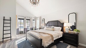 Une chambre avec un lit en bois foncé, une table de chevet avec une lampe, un miroir et une commode. Il y a une fenêtre avec des rideaux et une vue sur l’extérieur.