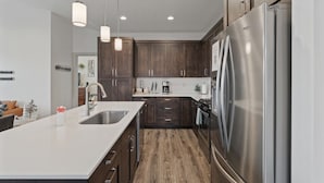 A modern kitchen with dark wood cabinets, stainless steel appliances, and pendant lighting.