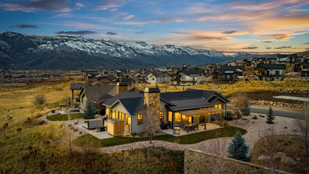 A residential area with modern houses, a well-maintained lawn, and a view of snow-capped mountains in the background.