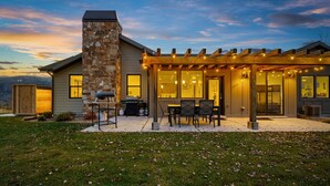A house with a stone chimney, a covered patio with outdoor seating, and a view of the mountains.