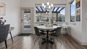 A dining area with a round table, chairs, a chandelier, and a view of a snowy landscape through large windows.