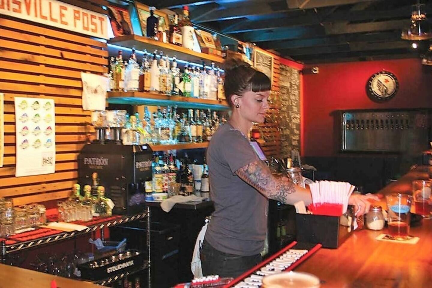 A bar with a wooden sign reading "SAVILLE POST" and a variety of liquor bottles on shelves.