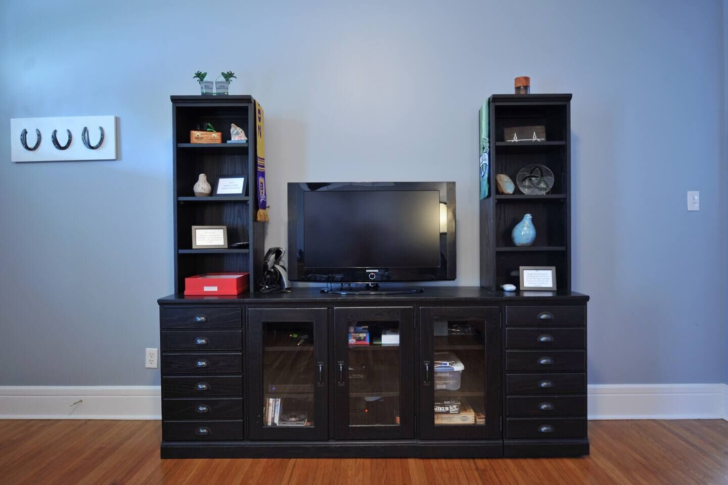A dark wood entertainment center with a flat-screen TV, two side cabinets, and a glass-fronted cabinet with storage.