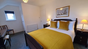 A hotel room with a large bed, two bedside tables with lamps, a chair, a radiator, a window with blinds, and a painting on the wall.
